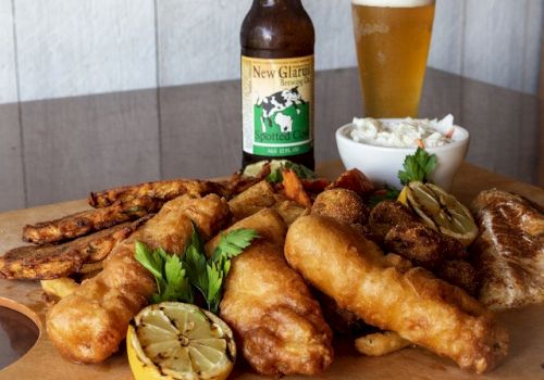 The image shows a meal of fried fish, lemon, fried sides, coleslaw, a bottle of New Glarus beer, and a glass of beer on a table. Ending the sentence.