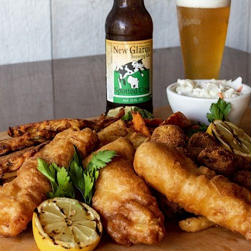 The image shows a meal of fried fish, lemon, fried sides, coleslaw, a bottle of New Glarus beer, and a glass of beer on a table. Ending the sentence.