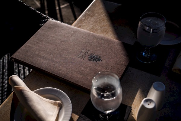 A menu on a table with two glasses of water, a napkin on a plate, and salt and pepper shakers.