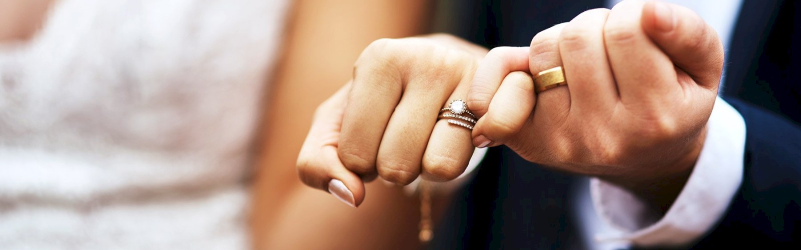 A close-up of two hands with wedding rings, showing a pinky-promise gesture, likely symbolizing a commitment or marriage.