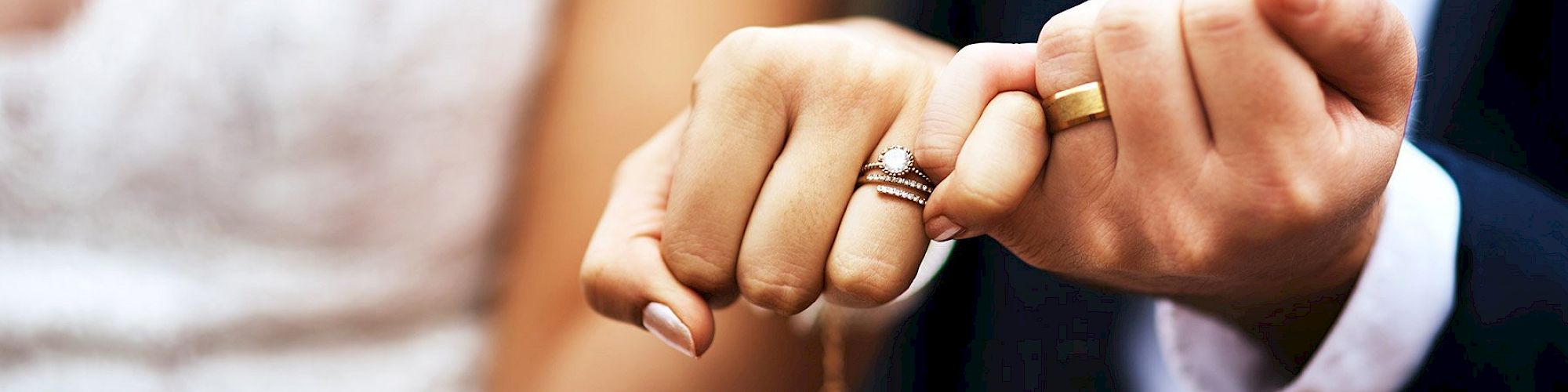 A close-up of two hands with wedding rings, showing a pinky-promise gesture, likely symbolizing a commitment or marriage.