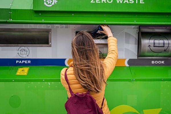 A person is recycling at a zero-waste station, depositing a book into the appropriate slot.
