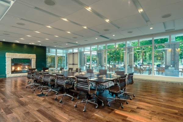 A modern conference room with a large table, chairs, and a fireplace, featuring large windows with an outdoor view.