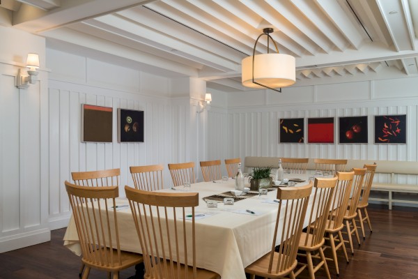 A conference room with a long table, wooden chairs, artwork on white walls, and soft lighting from overhead fixtures and wall lights.