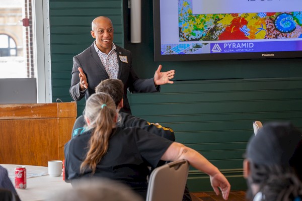 A speaker presents on a stage to an audience about inspired service at a professional event or seminar.