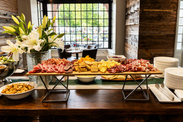 A cheese and charcuterie spread with flowers in a rustic restaurant setting for a brunch or buffet.