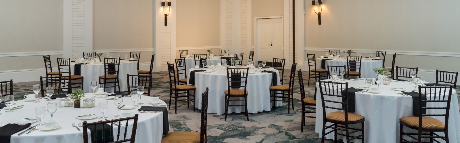 An elegant banquet hall with round tables, white tablecloths, and dark wooden chairs set for a formal event.