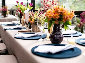 A beautifully set dining table with plates, napkins, wine glasses, and vibrant floral centerpieces in a bright and airy setting ends the sentence.