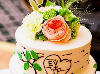 The image shows a decorated cake with floral accents and leaves. The cake has a heart with letters 