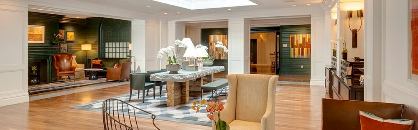 The image shows a spacious, stylishly furnished living area with a skylight, multiple seating arrangements, and warm lighting.