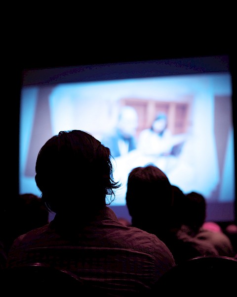 People sitting in a dark room watching a movie on a large screen.