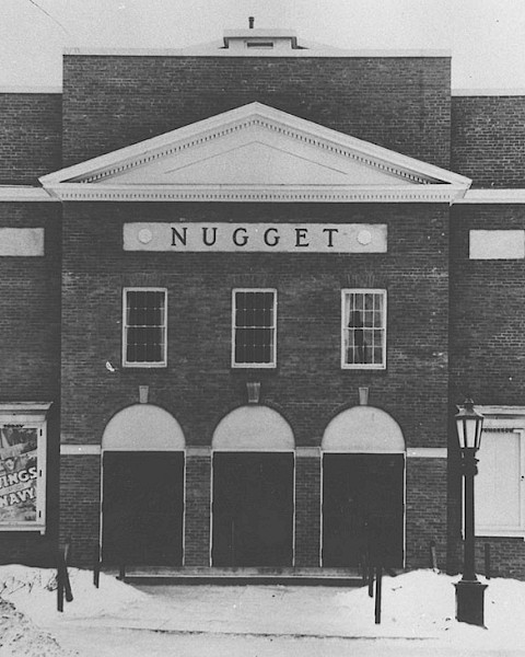 A vintage photo of the Nugget Theater building in winter, with a classic brick facade and snow-covered ground.