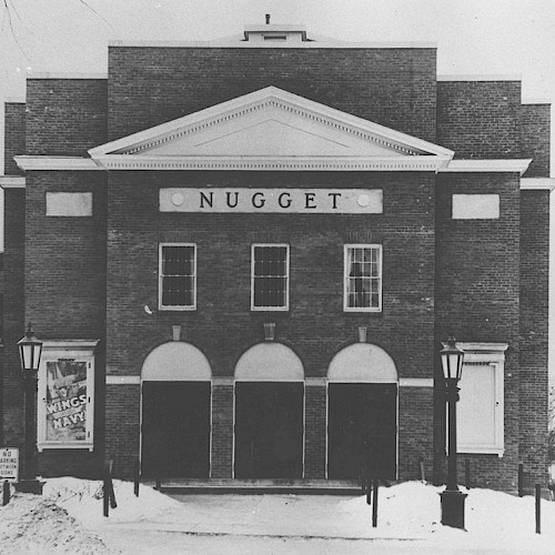 A vintage photo of the Nugget Theater building in winter, with a classic brick facade and snow-covered ground.