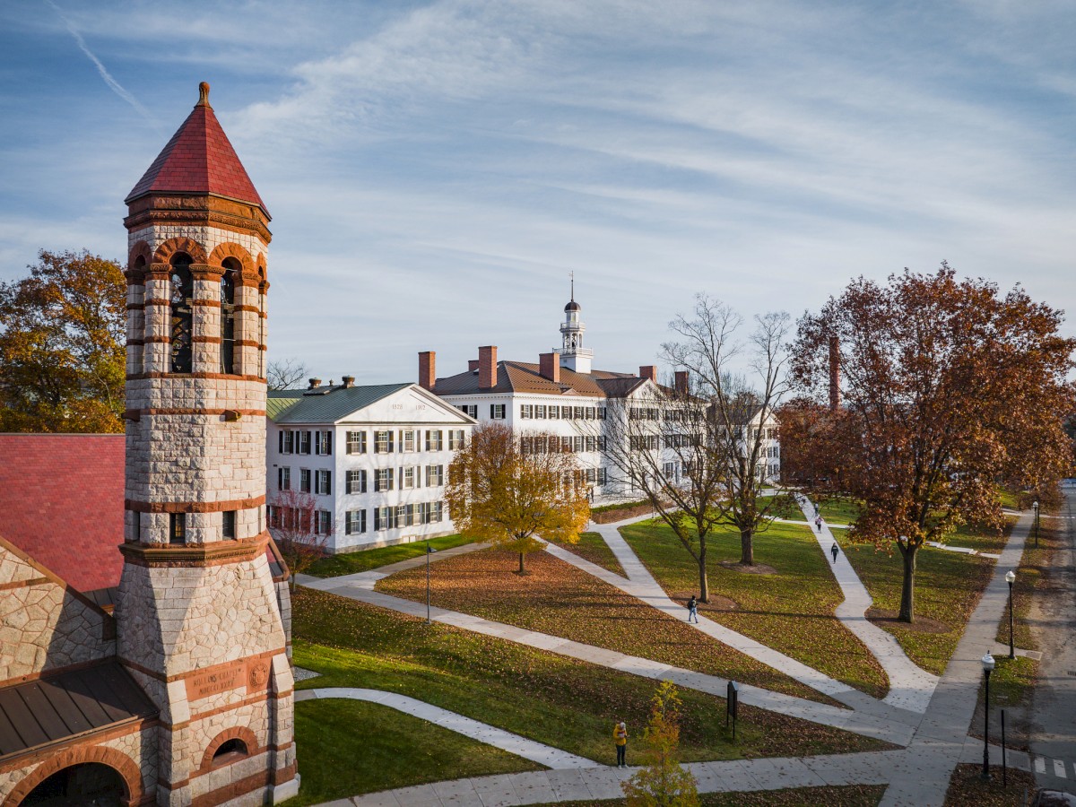 A historic building with a tower stands amidst green lawns and intersecting paths on a clear day.