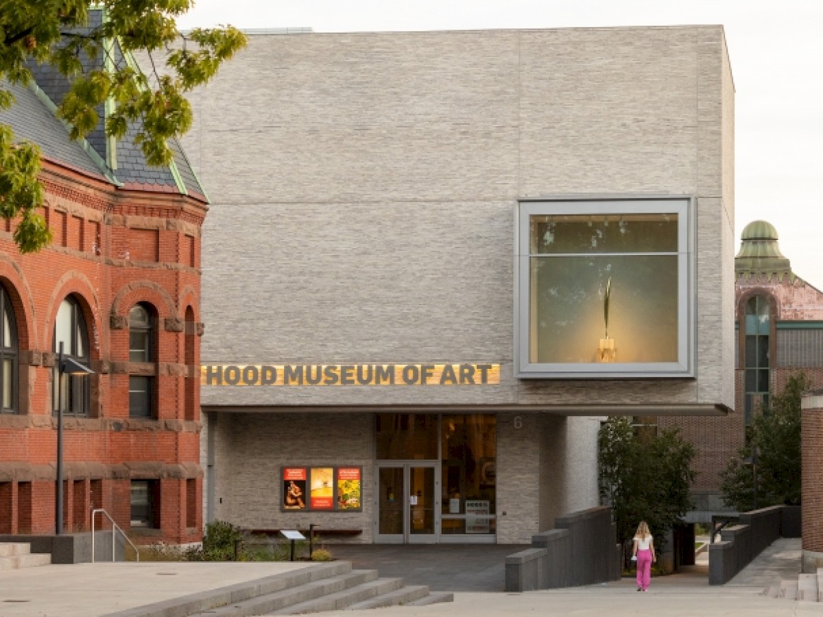 This image shows the Hood Museum of Art's modern building entrance, featuring art displays inside a window with brick and stone exterior walls.