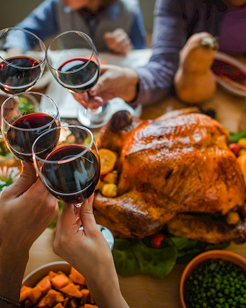 A festive meal with a roast turkey, various side dishes, and people toasting with red wine.