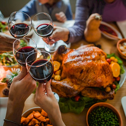 A festive meal with a roast turkey, various side dishes, and people toasting with red wine.