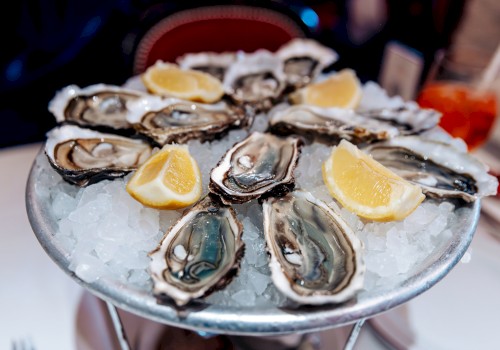 A plate of fresh oysters arranged on ice, garnished with lemon wedges, likely served as an appetizer or seafood dish.