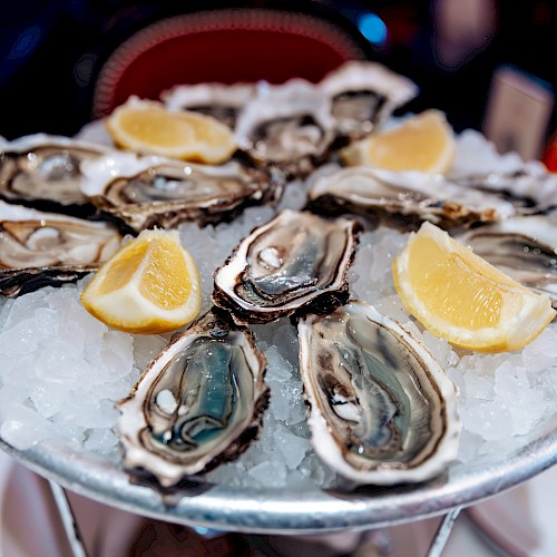 A plate of fresh oysters arranged on ice, garnished with lemon wedges, likely served as an appetizer or seafood dish.