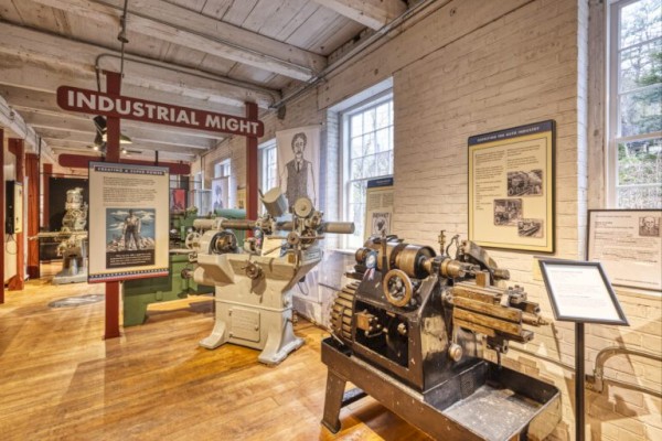 The image shows a museum exhibit with vintage industrial machinery and educational signs, titled 