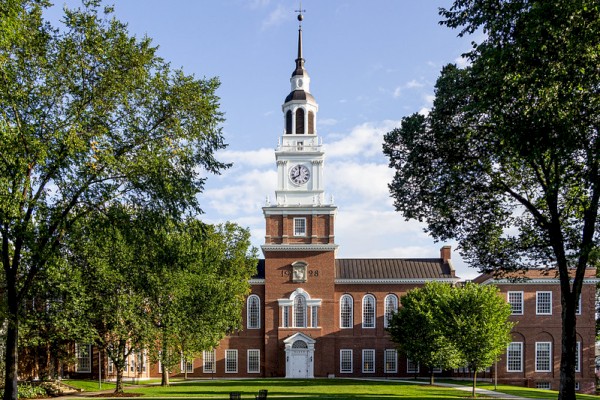 A brick building with a clock tower, surrounded by trees and grass, under a partly cloudy sky.