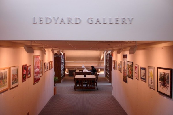 The image shows Ledyard Gallery, featuring artwork on the walls and a person seated at a table in the center of the room.