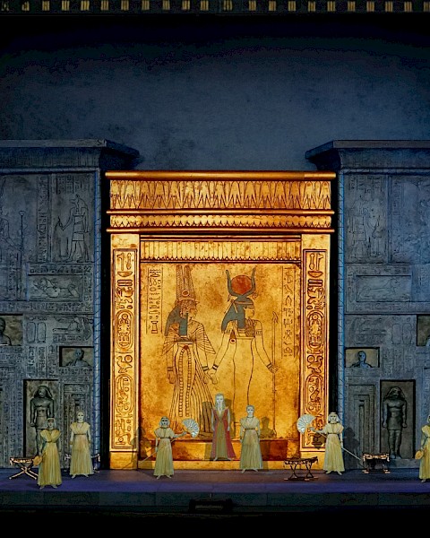 A stage set with an ancient Egyptian theme, featuring hieroglyphics, large golden doors, and performers in period costumes.