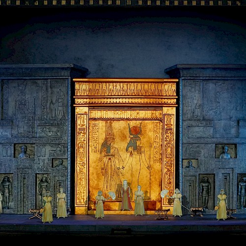 A stage set with an ancient Egyptian theme, featuring hieroglyphics, large golden doors, and performers in period costumes.