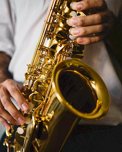 A person wearing a white shirt is holding and playing a shiny saxophone with both hands, focusing on the instrument.