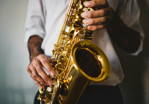 A person wearing a white shirt is holding and playing a shiny saxophone with both hands, focusing on the instrument.