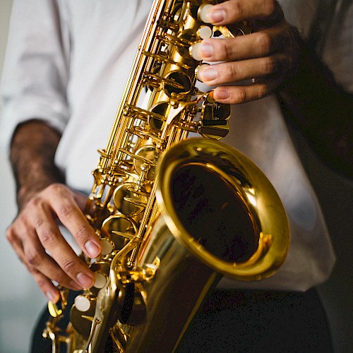 A person wearing a white shirt is holding and playing a shiny saxophone with both hands, focusing on the instrument.