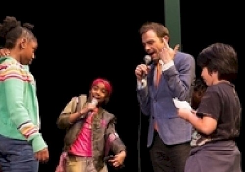 A group of people are on stage with microphones, appearing to engage in a lively conversation or performance.