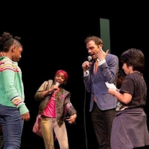 A group of people are on stage with microphones, appearing to engage in a lively conversation or performance.