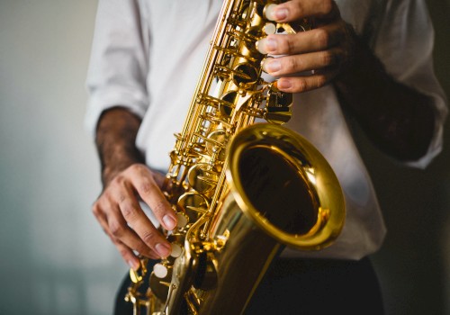 A person is holding and playing a saxophone, wearing a white shirt, against a neutral background.