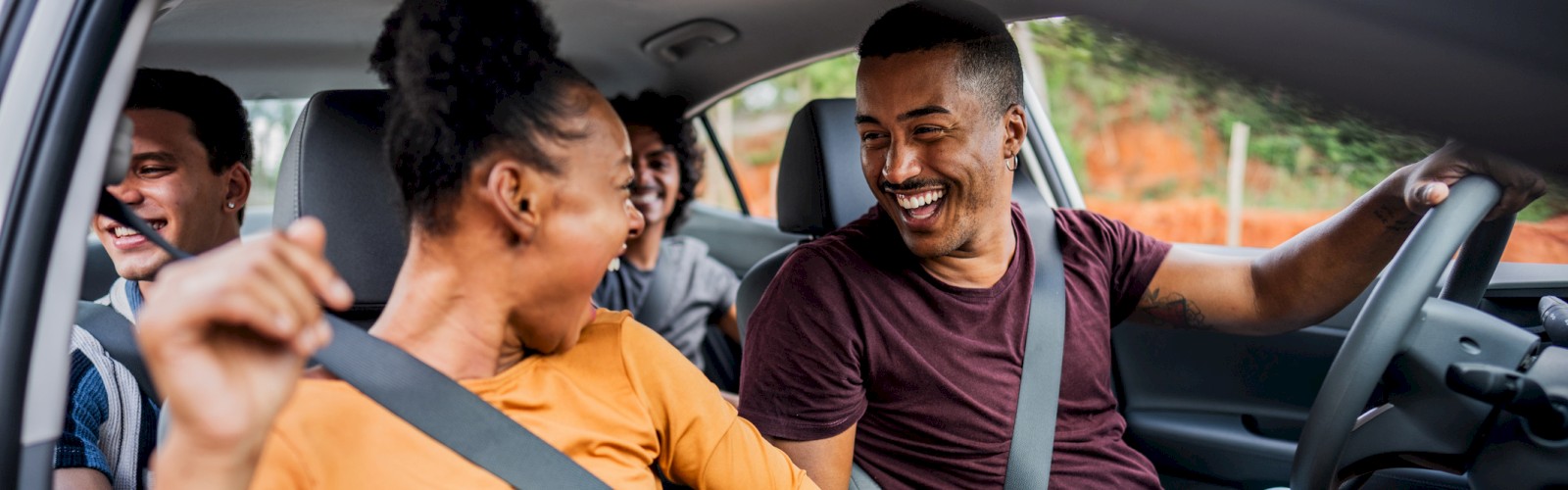 A group of people in a car having fun, with two in the front seat smiling and laughing, and two in the back seat enjoying the ride.