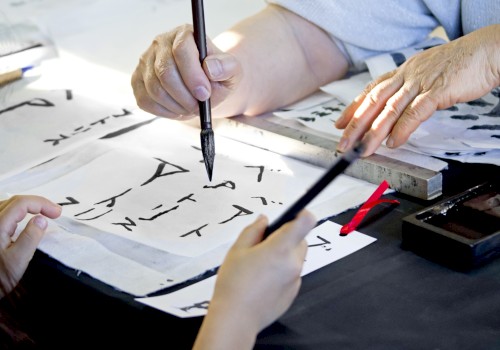 People practicing calligraphy with brushes and ink, creating text on white paper, focusing on traditional writing techniques.