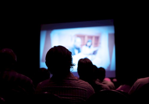 A group of people are watching a blurry projection in a dark room, indicating a movie or presentation.