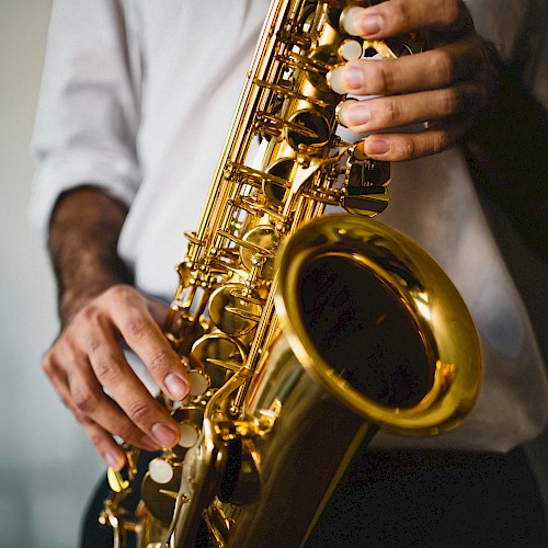 A person wearing a white shirt is playing a saxophone. Their hands are positioned on the keys of the shiny brass instrument.