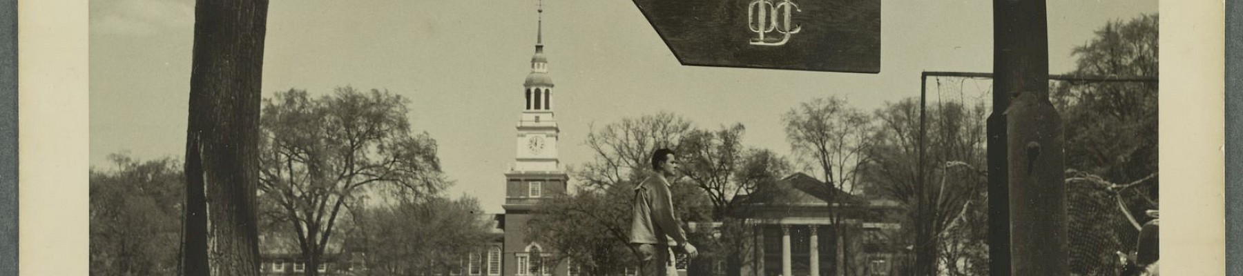 The image shows a path with a directional signpost, tall trees, and a building with a tower in the background, under a clear sky.