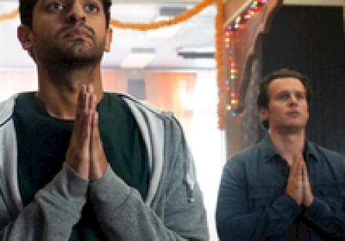 Two people stand inside a decorated room with their hands in a prayer position, looking upwards.