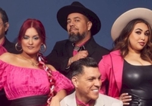 A group of people posing, wearing pink and black outfits with hats. They stand against a plain background, exuding a stylish and confident vibe.