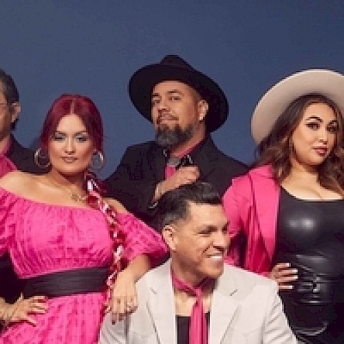 A group of people posing, wearing pink and black outfits with hats. They stand against a plain background, exuding a stylish and confident vibe.