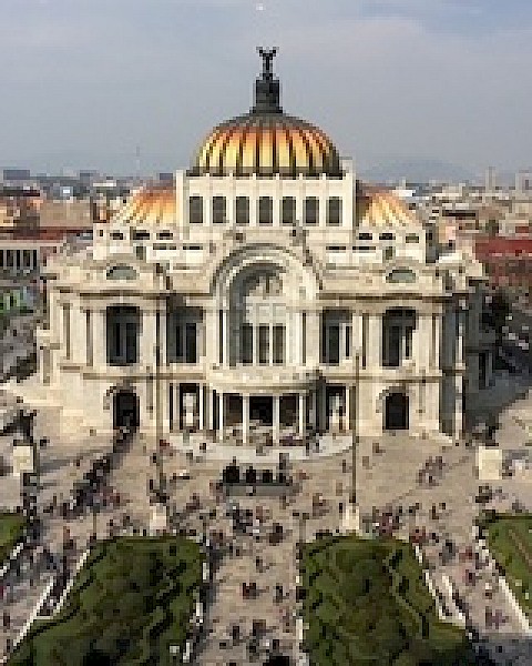 The image shows a grand building with a golden dome, marble architecture, and a busy public square in front, set in an urban environment.