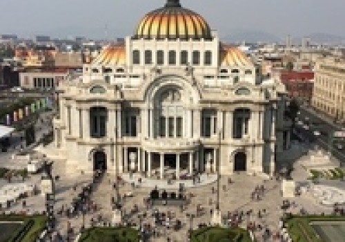 The image shows a grand building with a golden dome, marble architecture, and a busy public square in front, set in an urban environment.