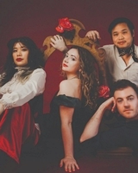 A group of four people in theatrical attire pose confidently against a dark red background.