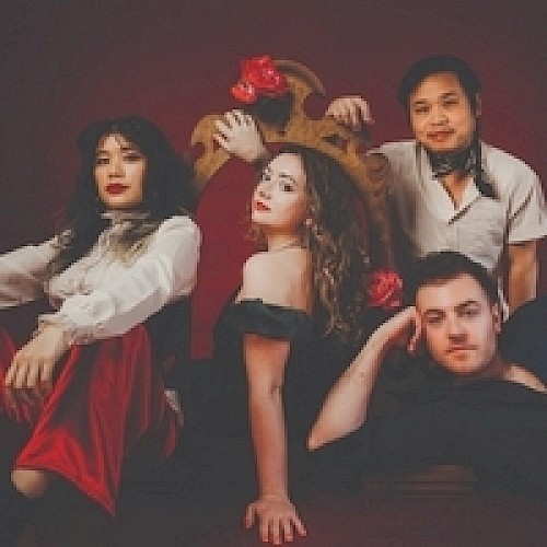 A group of four people in theatrical attire pose confidently against a dark red background.