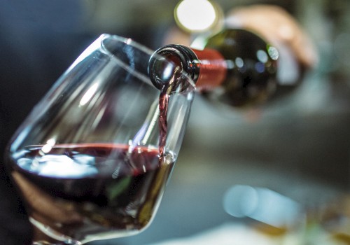 A glass is being filled with red wine poured from a bottle, with a blurred background.