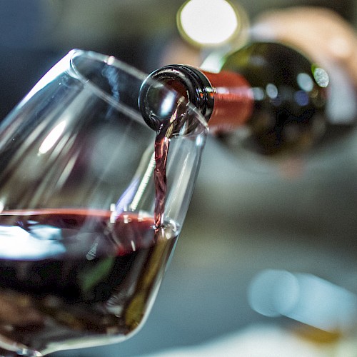 A glass is being filled with red wine poured from a bottle, with a blurred background.