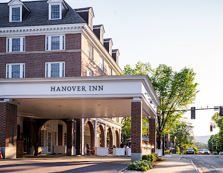 The image shows the entrance of Hanover Inn, a brick building with a covered driveway, trees, and a street with traffic lights nearby.