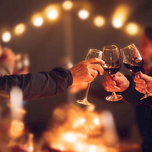 People are toasting with wine glasses in a warmly lit, festive setting, creating a cheerful and celebratory atmosphere.